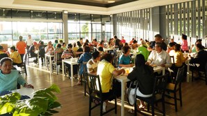 Un'ampia sala da pranzo con diversi tavoli e sedie, grandi finestre che lasciano entrare la luce naturale e lampadari a sospensione.