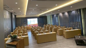 Una sala conferenze con file di tavoli e sedie, dotata di microfoni e bottiglie d'acqua.