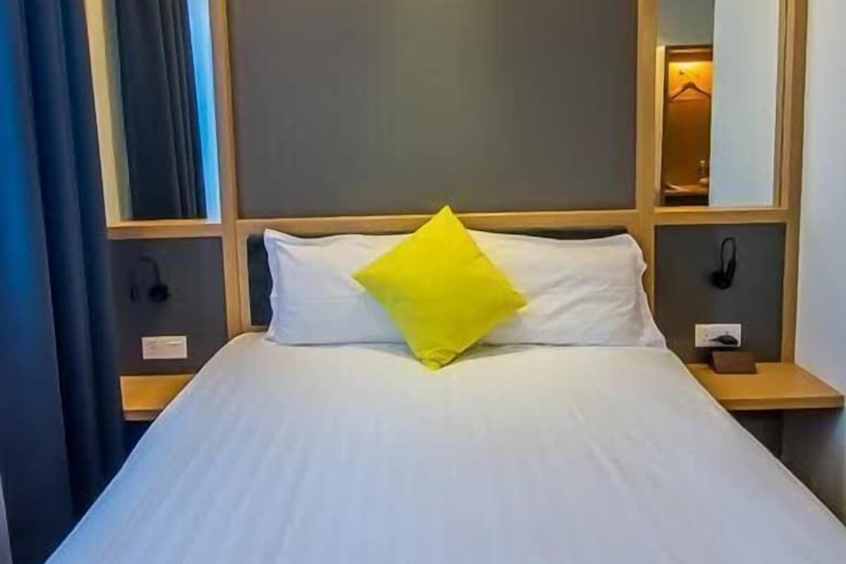 A hotel room with a bed, a nightstand, a mirror, and a curtain.