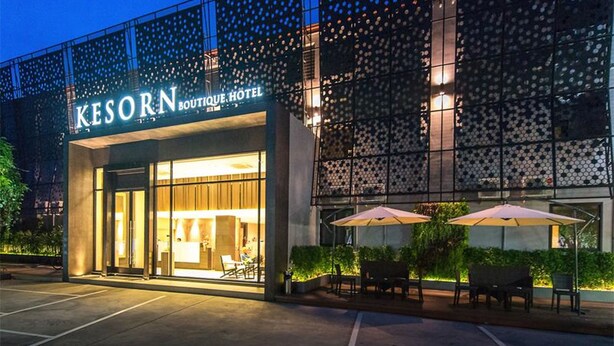 The exterior of the Kesorn Boutique Hotel with a modern design, featuring large glass windows and outdoor seating with umbrellas. - Kesornboutique Hotel (Buriram)