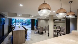 A modern hotel lobby with a central bar area, dining space, and large windows offering a view of the outside. - Kesornboutique Hotel (Buriram)