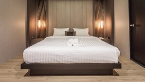 A modern bedroom with a skylight, a large bed, two bedside tables, and a dark door. - Kesornboutique Hotel (Buriram)