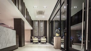 A modern hotel lobby with a marble reception desk, seating area, and large windows offering views of the outdoors. - Kesornboutique Hotel (Buriram)