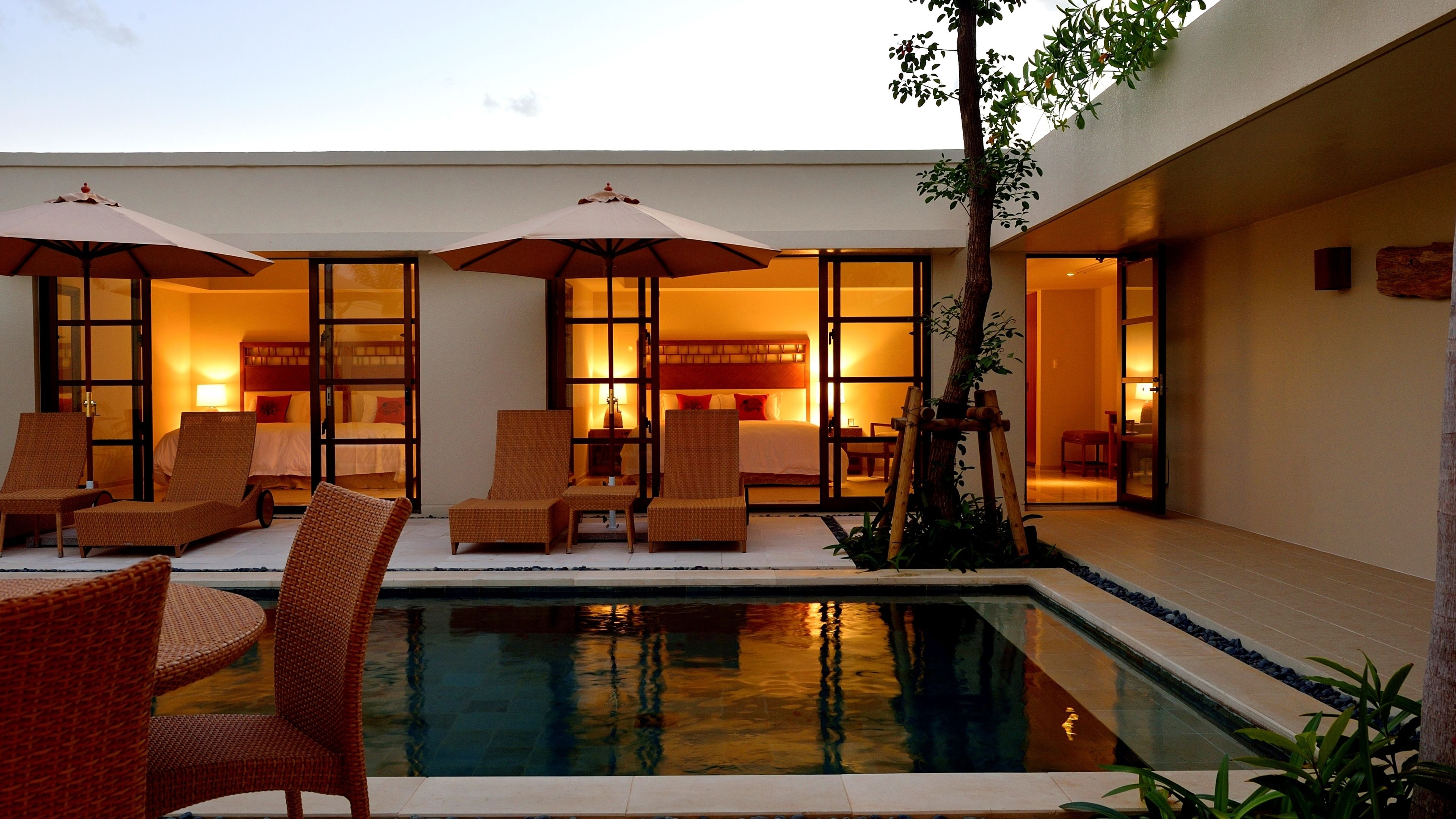 A hotel room with a pool, lounge chairs, and umbrellas.
