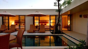 A hotel room with a pool, lounge chairs, and umbrellas.