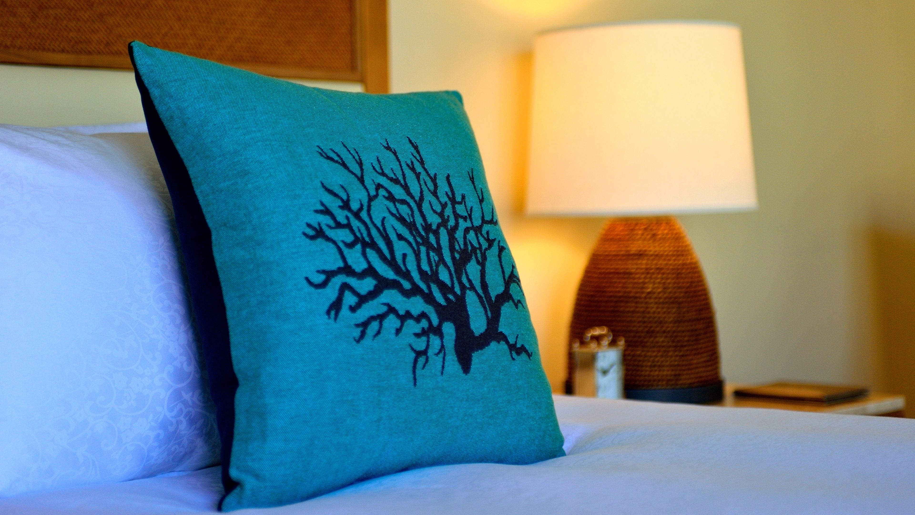 Ein Bett mit einem türkisfarbenen Kissen mit einem schwarzen Baumdesign, einem weißen Kissen und einem Nachttisch aus Holz mit einer Lampe.