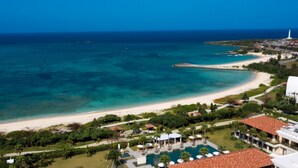 An aerial view of a coastal resort with a beach, swimming pool, and lush greenery. - The Uza Terrace Beach Club Villas (Yomitan)