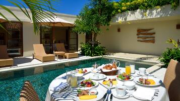 A poolside breakfast setup with a table, chairs, and a pool.