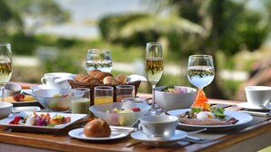 A table set with breakfast items, including bread, fruit, and beverages, with a view of greenery in the background. - The Uza Terrace Beach Club Villas (Yomitan)