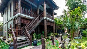 A traditional wooden house with a wooden staircase leading to a balcony, surrounded by lush greenery and potted plants. - JAVA WOODEN VILLA (Siem Reap)
