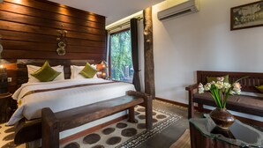 A bedroom with a wooden headboard, a large bed with green pillows, a glass coffee table with a vase of flowers, and a bench. - JAVA WOODEN VILLA (Siem Reap)