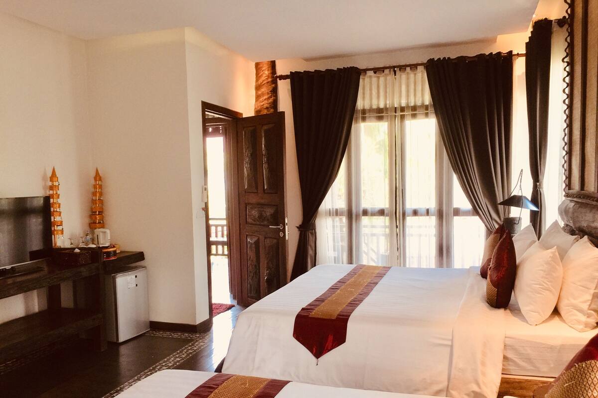 A hotel room with two beds, a desk with a computer, a television, and a window with curtains.