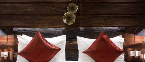 Un lit avec une literie blanche et des oreillers rouges, un plafond en bois et un élément décoratif suspendu.