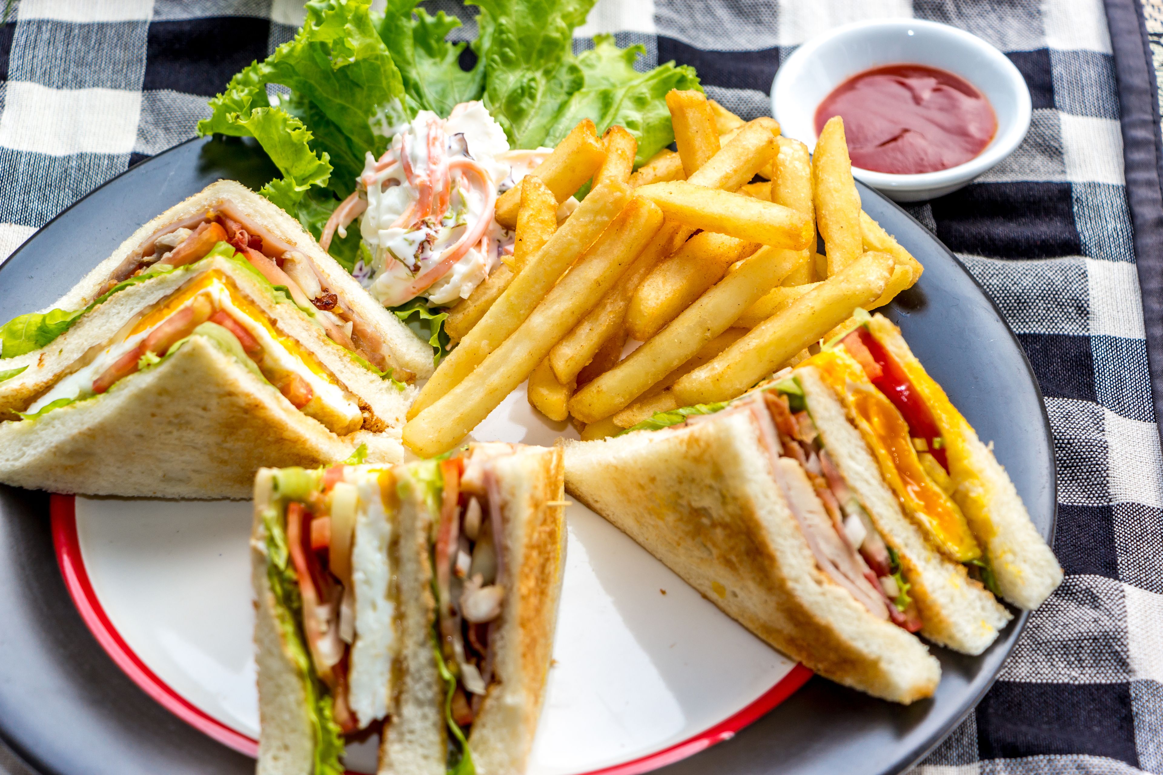 Ein Teller mit einem in Dreiecke geschnittenem Sandwich, Pommes und einem gemischten Salat mit einer kleinen Ketchup-Schale.