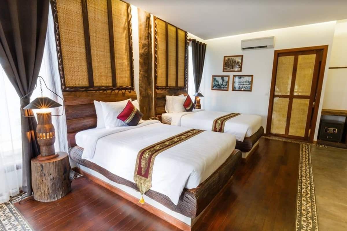 A hotel room with two beds, a wooden headboard, a traditional lamp, and a large window with curtains.