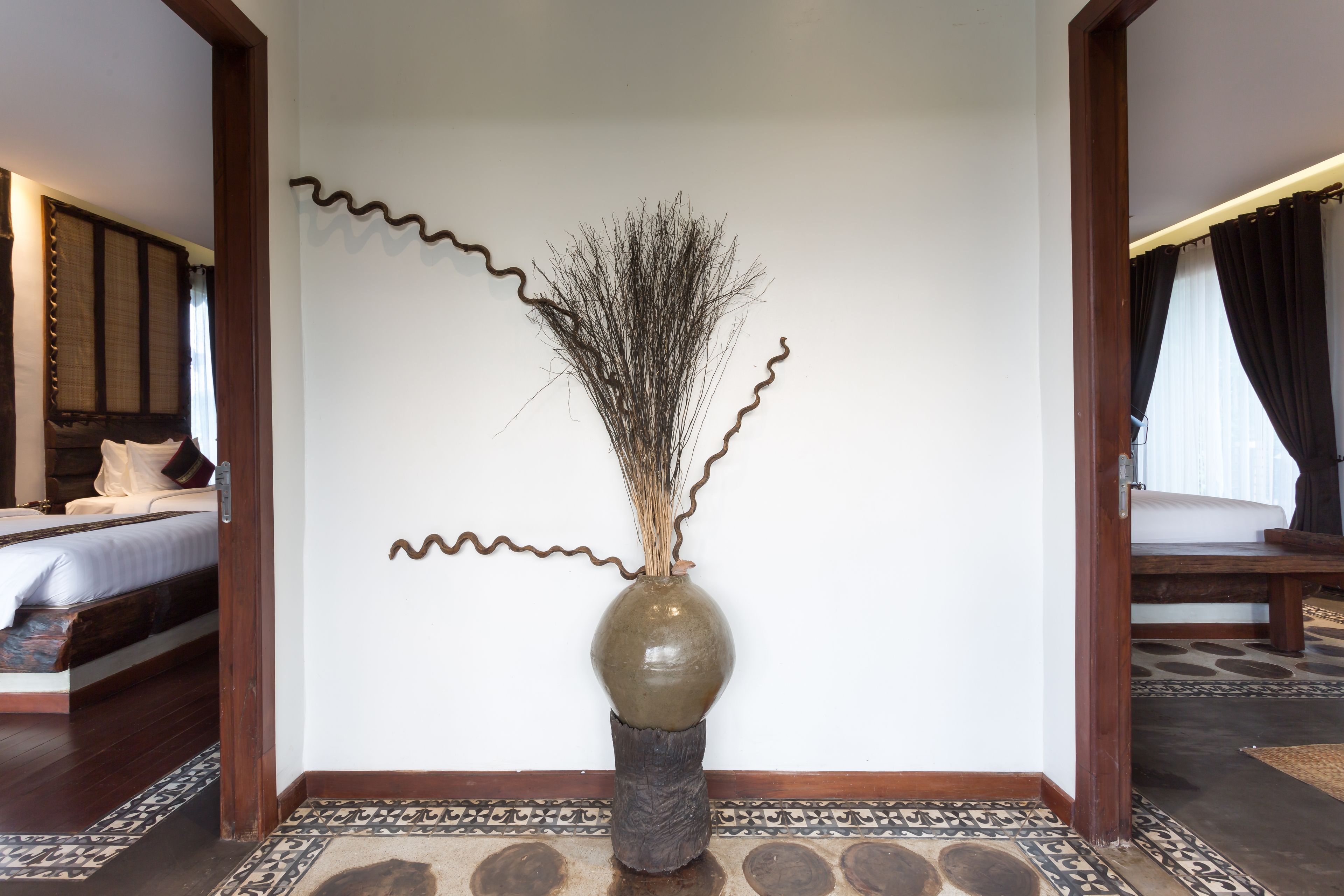 A room with a bed, a vase with branches, and a patterned floor.