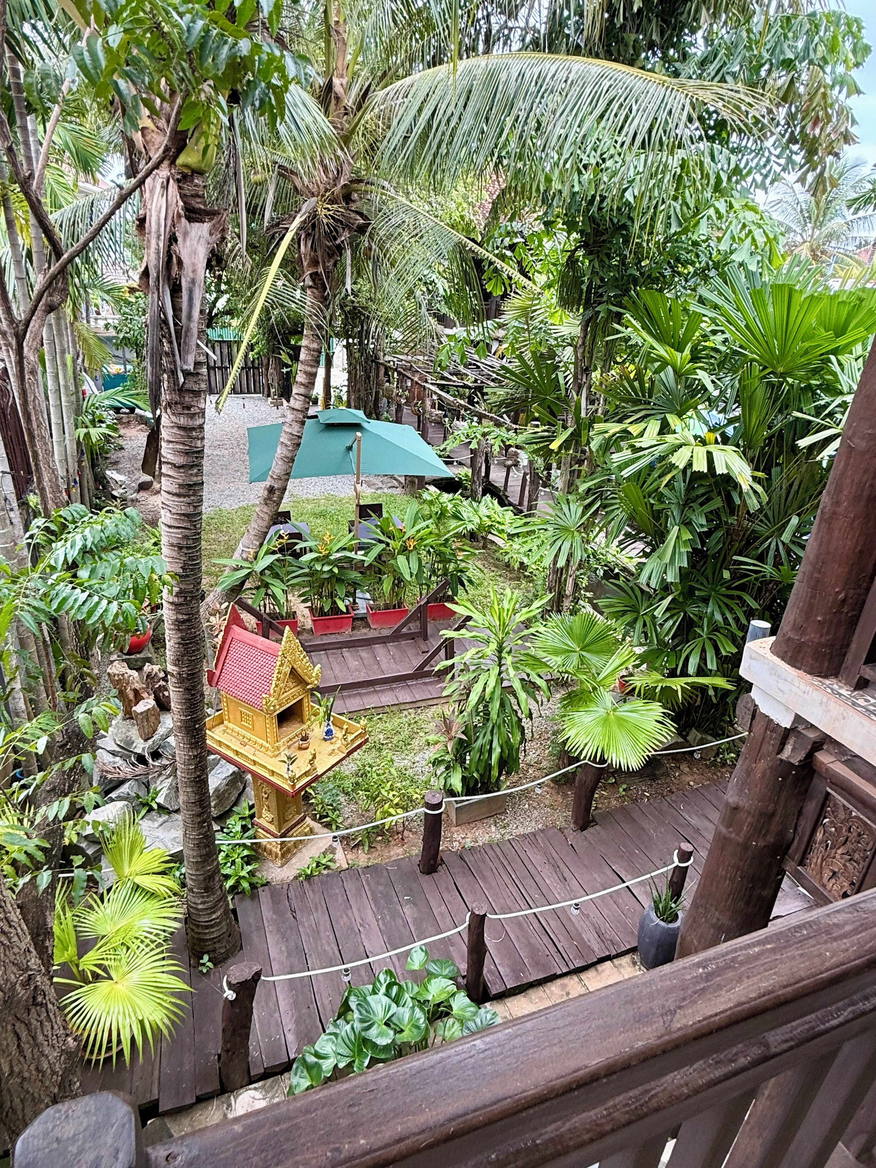 Una terraza de madera con un pequeño santuario y abundante vegetación tropical.