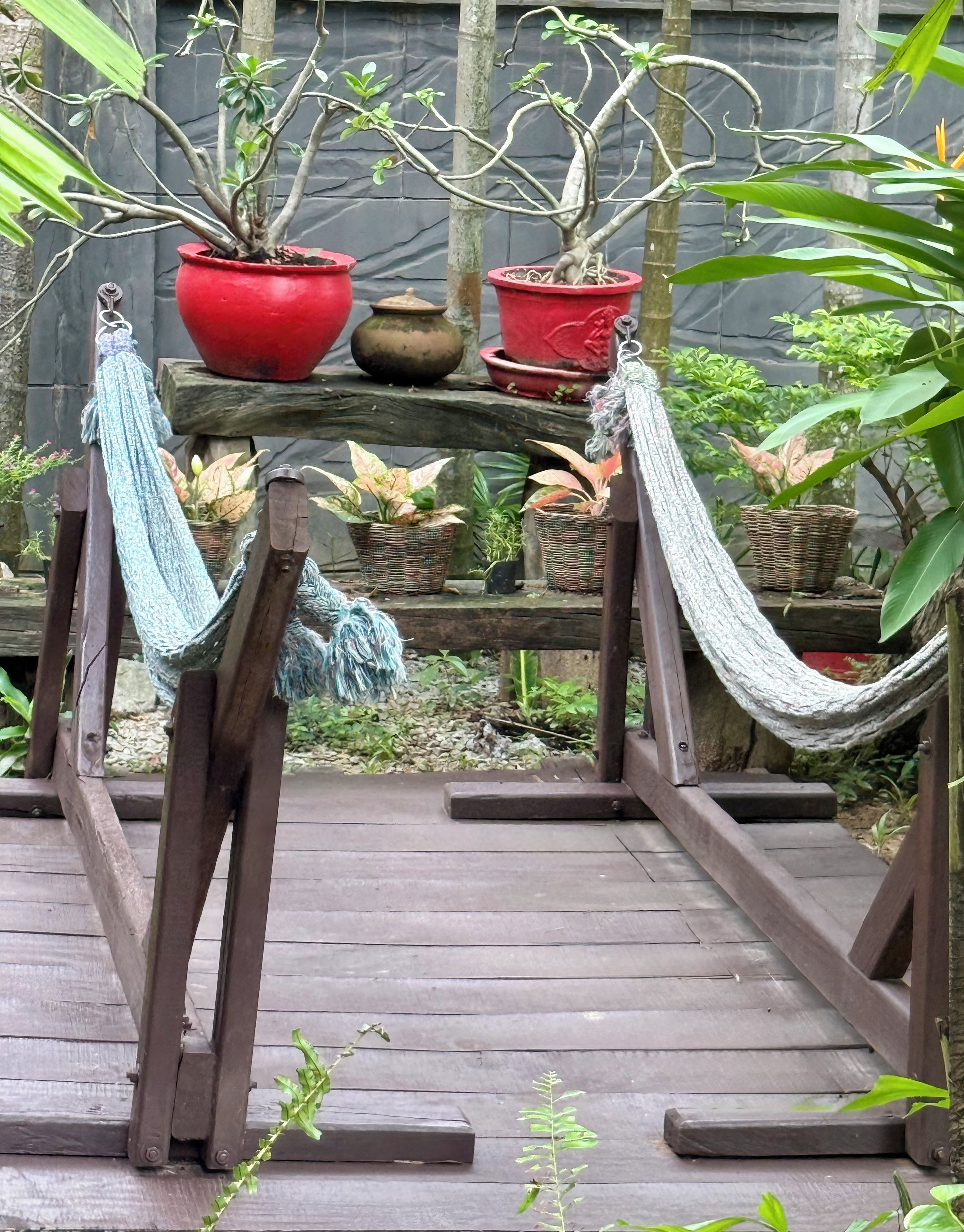 Una terraza de madera con una hamaca, plantas en macetas y una baranda de madera rústica.