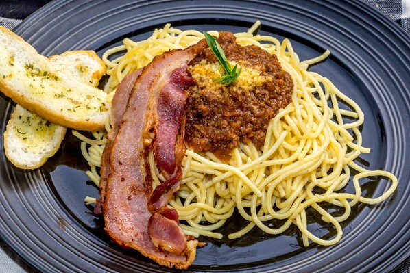 A plate of spaghetti with a piece of bacon and a garnish on top.