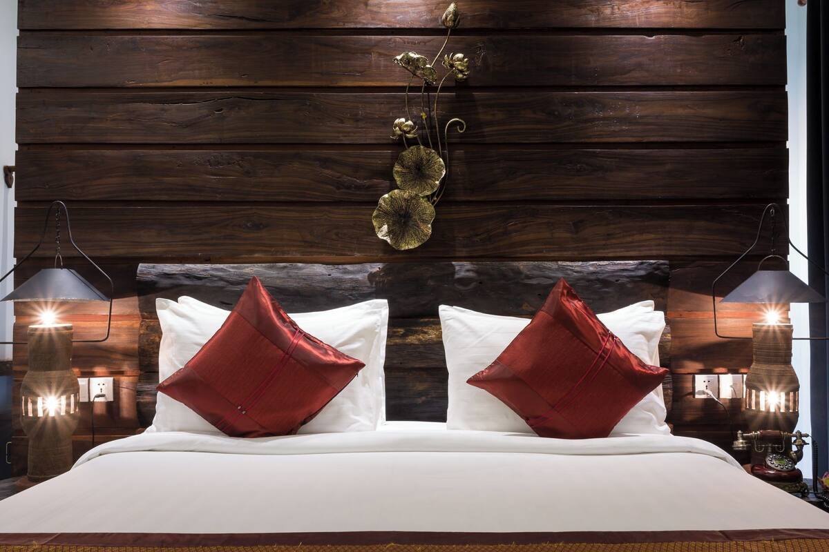 A bed with white linens and red pillows, a wooden headboard, and wall-mounted lamps.
