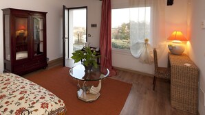 A bedroom with a bed, a glass-top table with a potted plant, a wicker side table with a lamp, a wooden cabinet, and a window with curtains. - Agriturismo La Gironda (Forlì)
