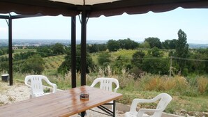 An outdoor patio with a wooden table and white plastic chairs, overlooking a scenic landscape. - Agriturismo La Gironda (Forlì)