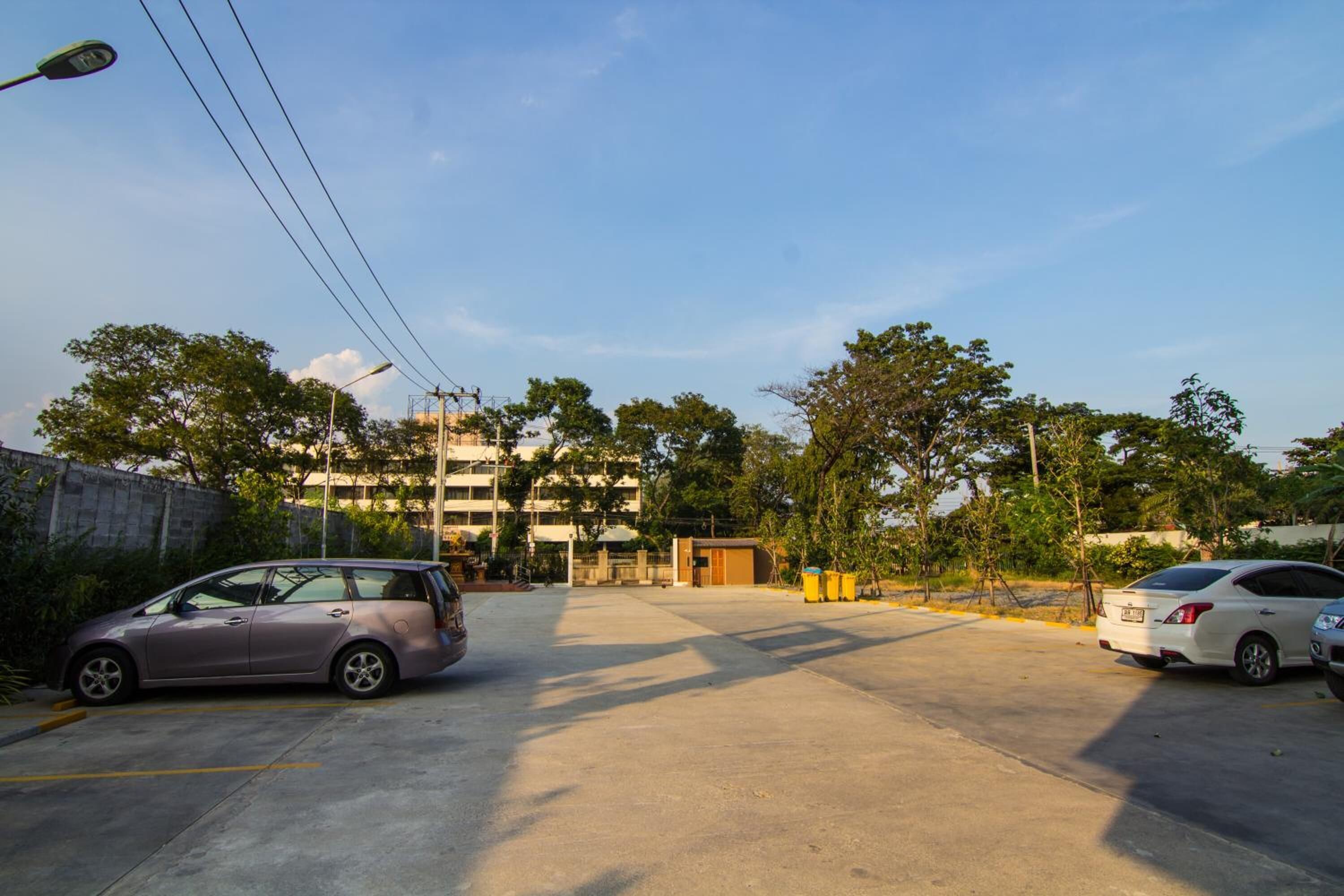 A parking lot with two cars, a building in the background, and trees around.