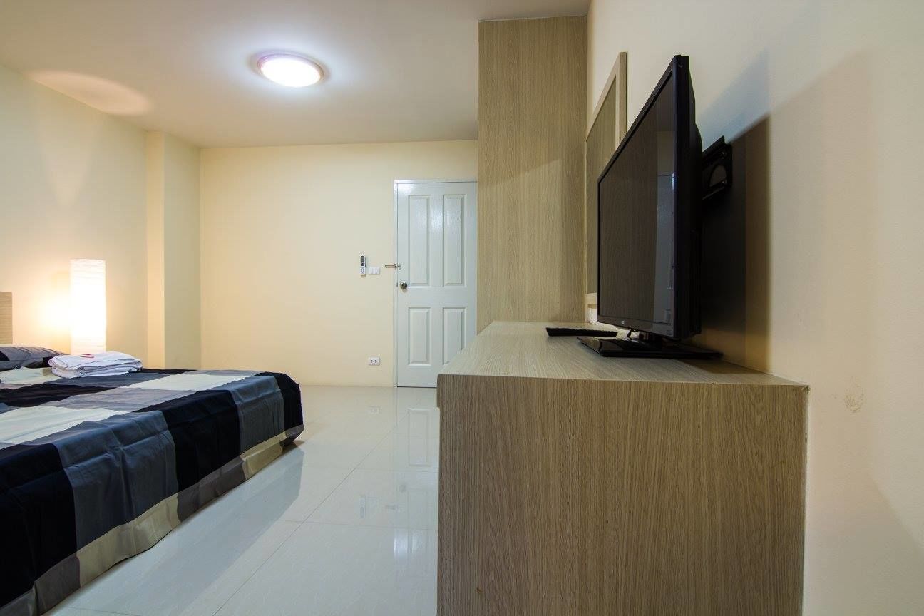 A hotel room with a bed, a TV on a stand, and a door in the background.
