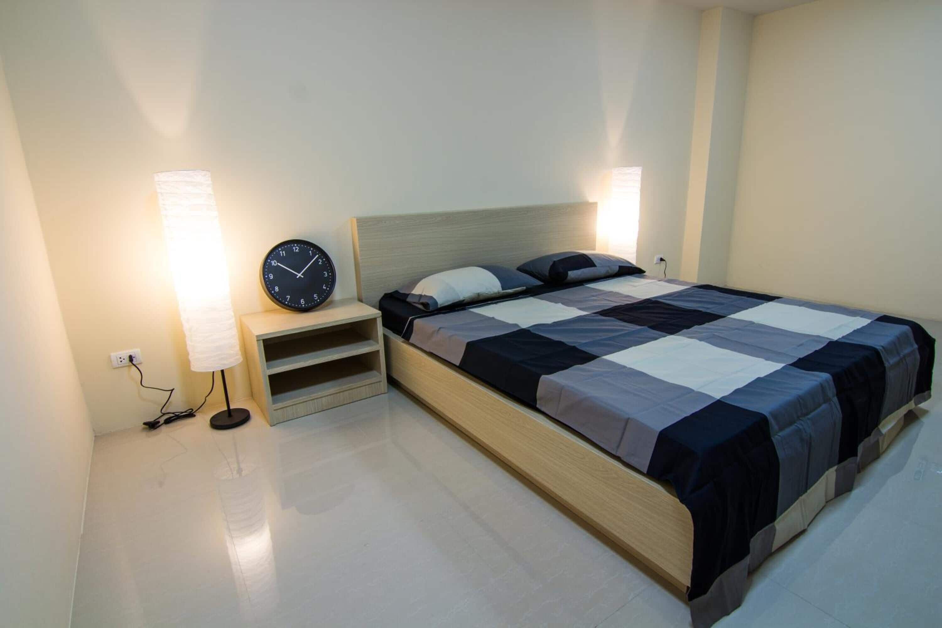 A modern bedroom with a wooden bed, a nightstand with a clock, and a wall-mounted lamp.