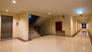 A spacious, well-lit hallway with a modern elevator, a staircase, and a red emergency exit sign. - Dae Ma Place (Nonthaburi)