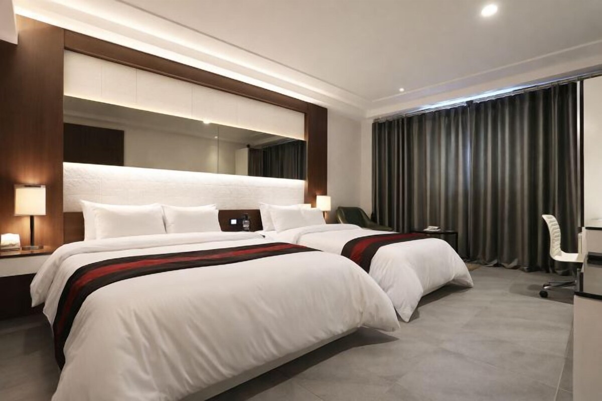 A hotel room with two beds, a desk, a chair, and a large mirror.