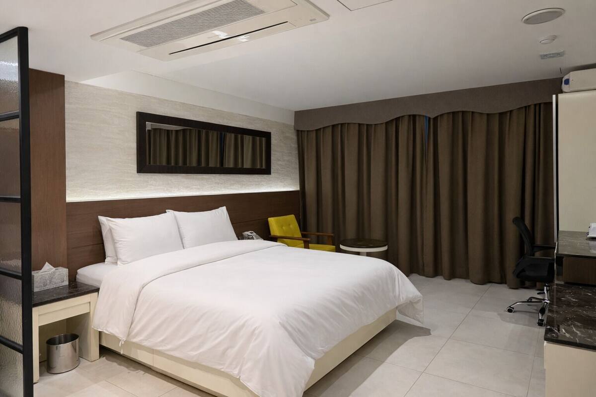 A modern hotel room with a large bed, a desk, a chair, and a mirror on the wall.