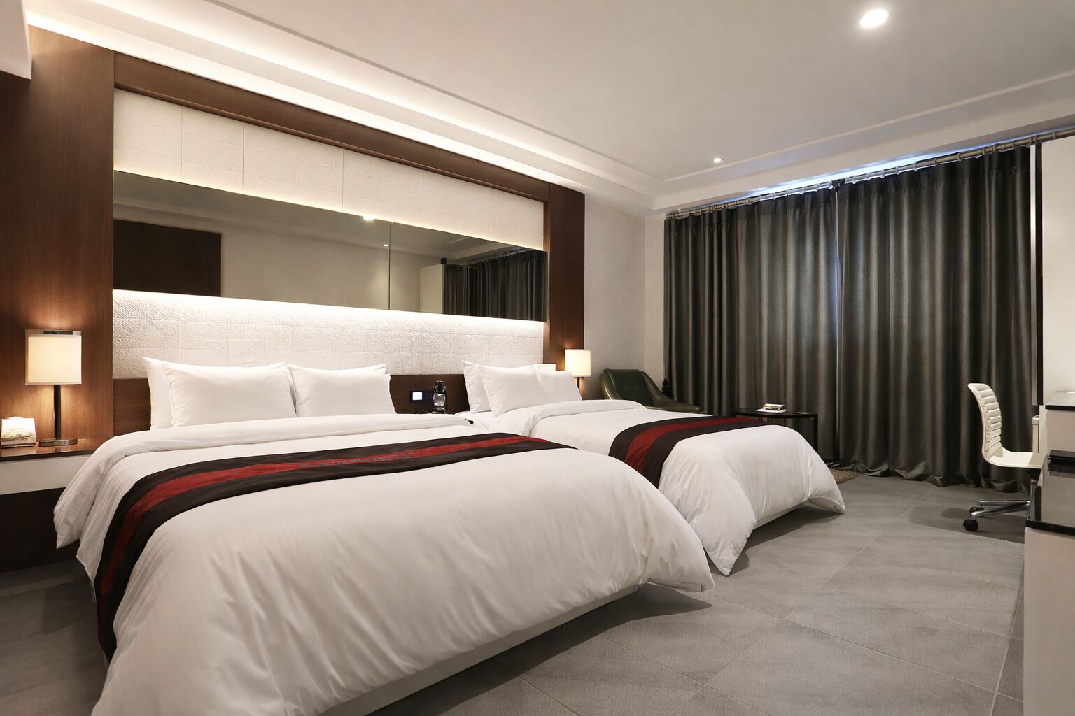 Ein modernes Hotelzimmer mit zwei Betten, einem großen Spiegel, einem Schreibtisch und einem Stuhl.