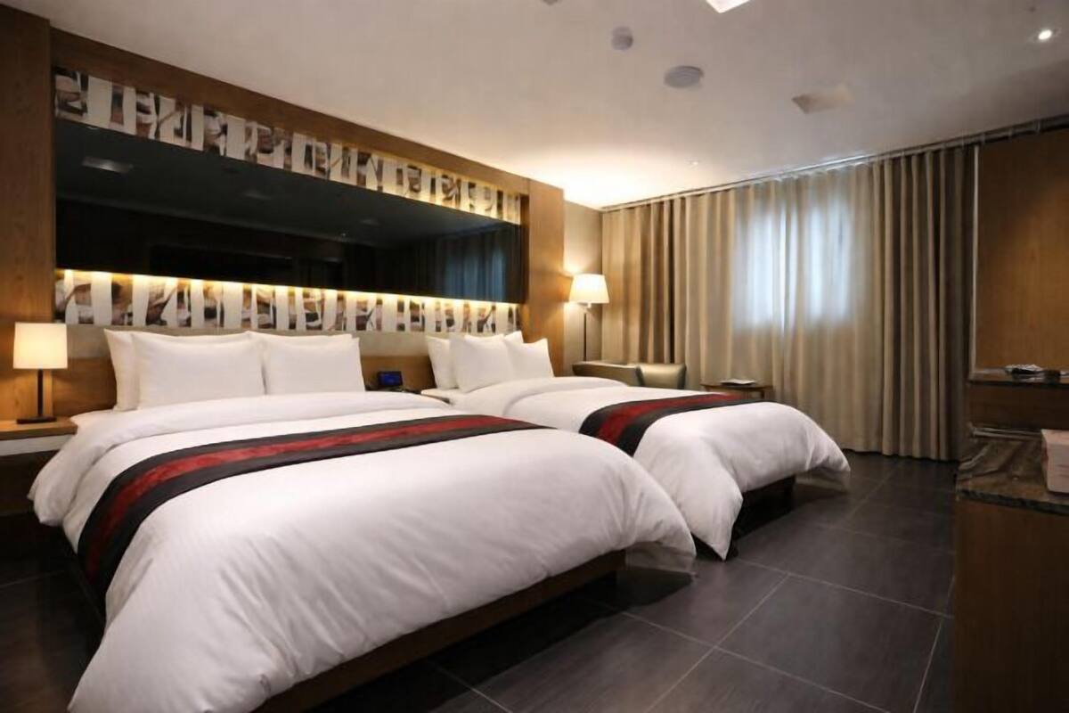 A hotel room with two beds, a large mirror, a desk, and a window with curtains.