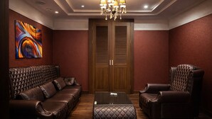 A room with a leather sofa, a high-backed chair, a glass coffee table, and a wooden door with louvered panels. - Zenith Hotel (Bucheon)