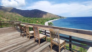 A wooden deck with chairs overlooking a beach and mountains. - Wawa Wewe Rock (Karangasem)