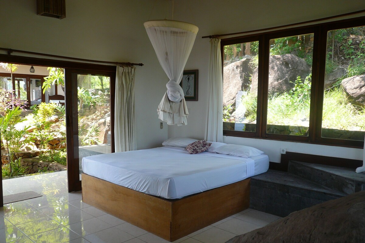 Un dormitorio con cama, dosel colgante, vistas al exterior y un banco de piedra.