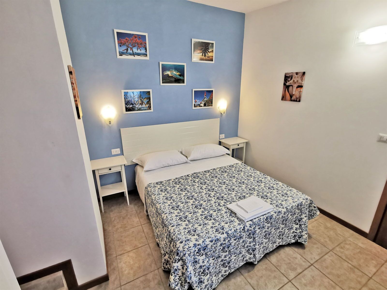 Un dormitorio con una cama, dos mesitas de noche y cuatro cuadros colgados en la pared.
