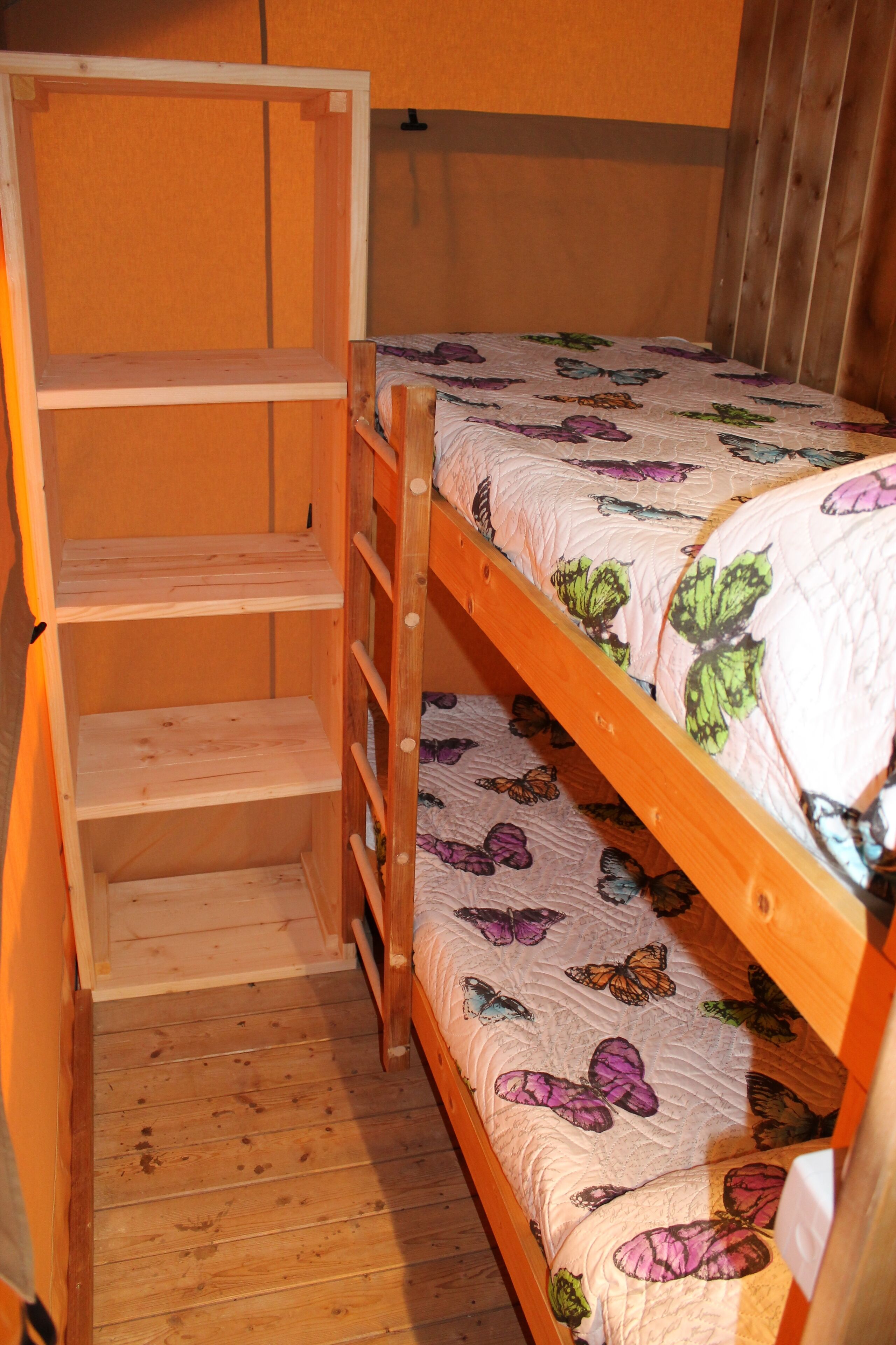 Un letto a castello con copripiumino a tema farfalle, una scala in legno e una scaffalatura.