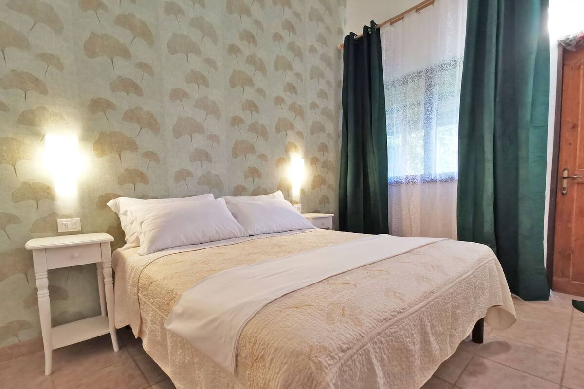 A neatly made bed with a white bedspread and pillows, a small bedside table, and a wall with a leaf pattern.