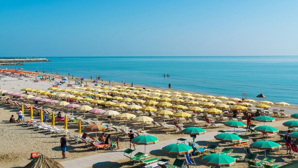 A beach with rows of sun umbrellas and lounge chairs, a clear sky, and calm sea. - Il Girasole (Massignano)