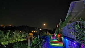 A nighttime garden pathway with colorful lighting, a wooden playhouse, and a view of distant hills. - Il Girasole (Massignano)