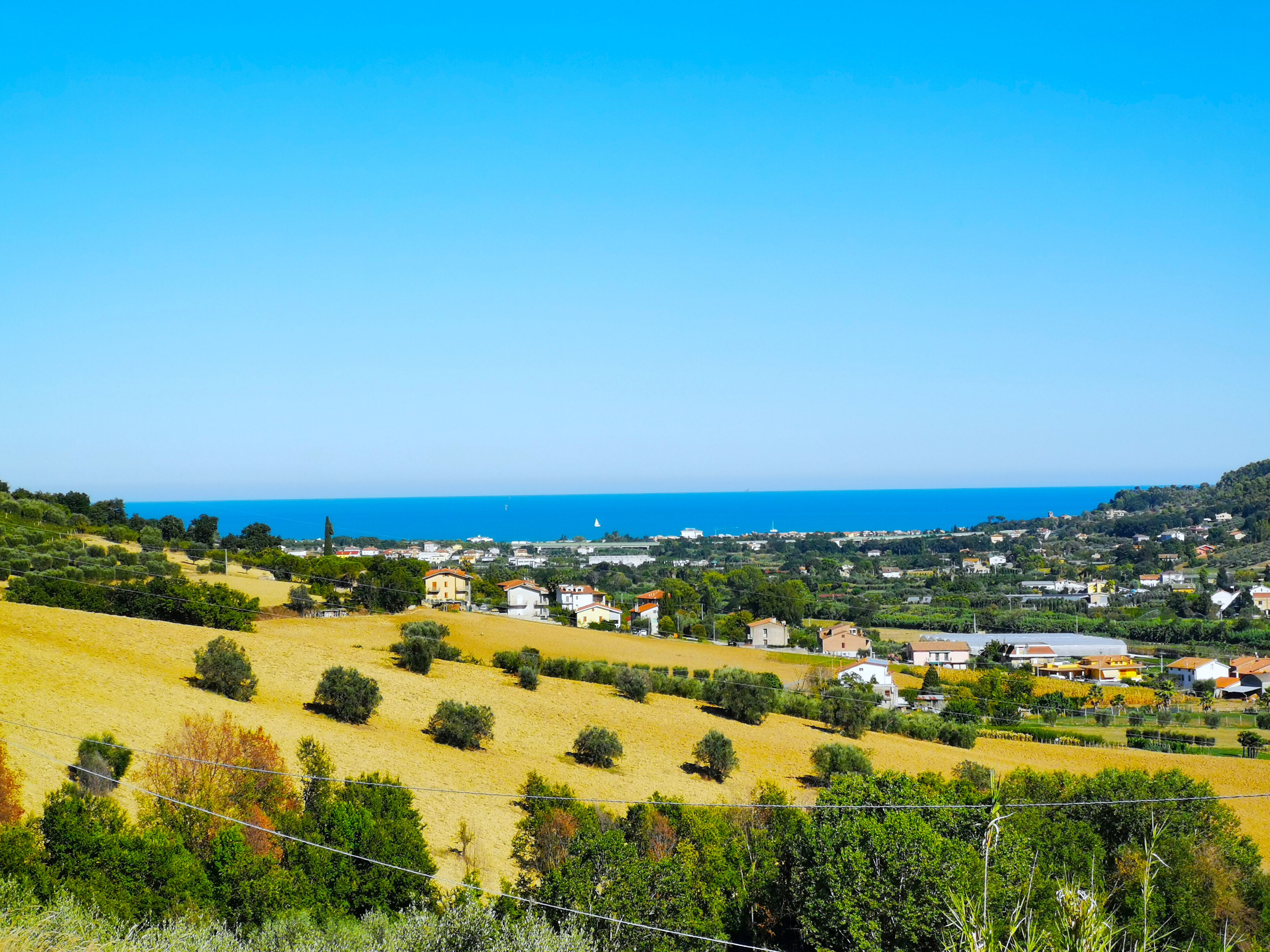 A coastal town with houses on a hillside, a clear blue sky, and the sea in the distance.