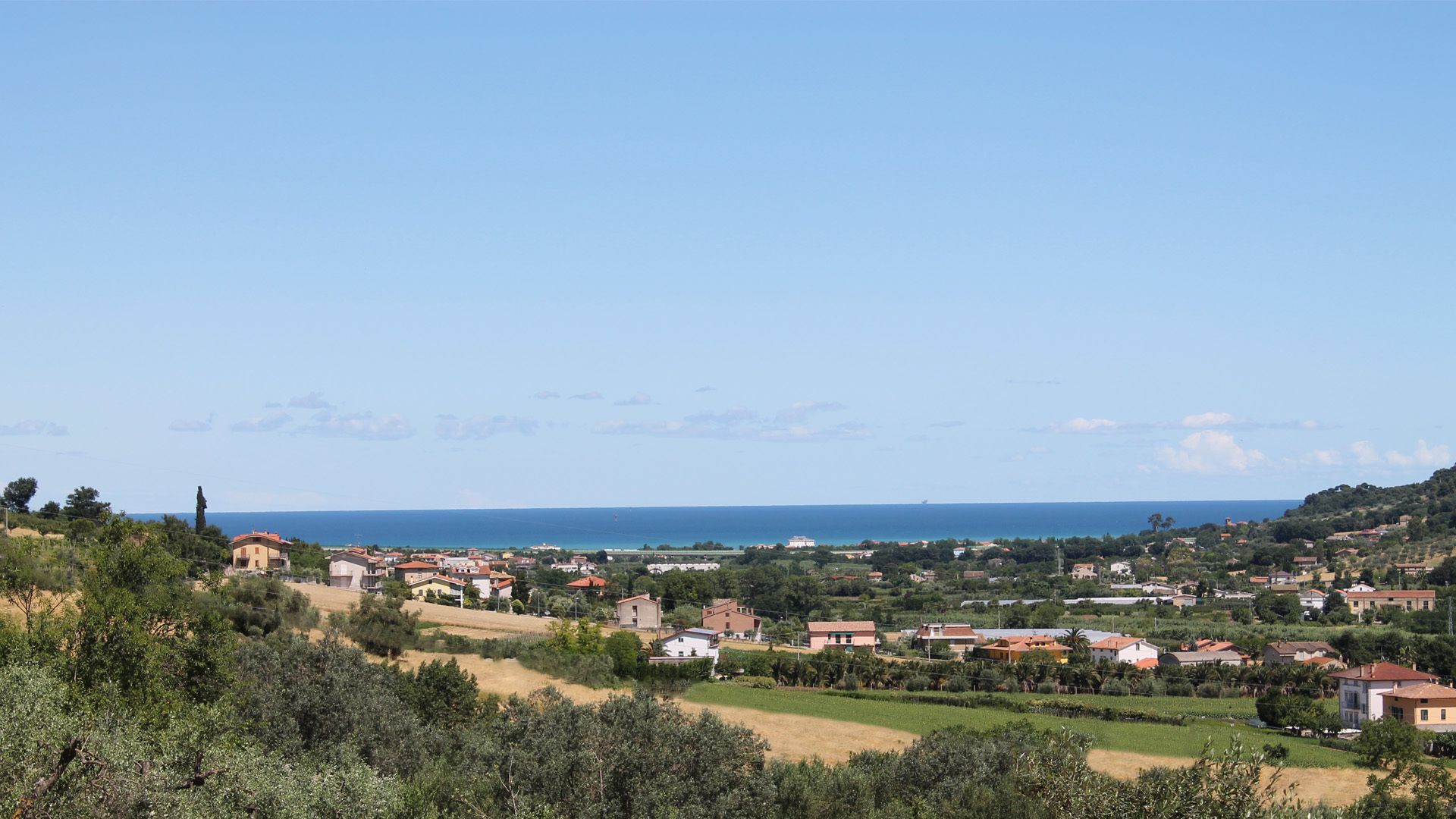 Eine Küstenstadt mit Häusern, Feldern und freiem Blick auf das Meer.