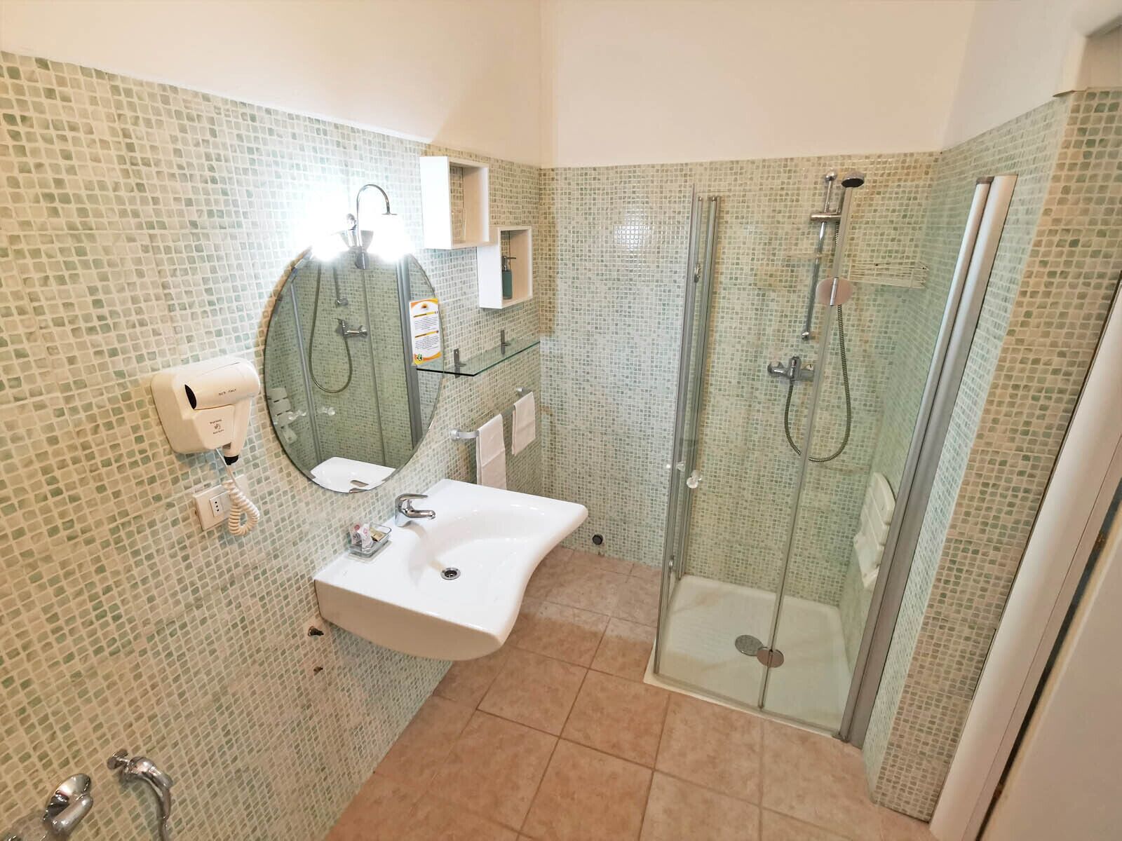 A bathroom with a glass-enclosed shower, a sink with a mirror, and a hand dryer.