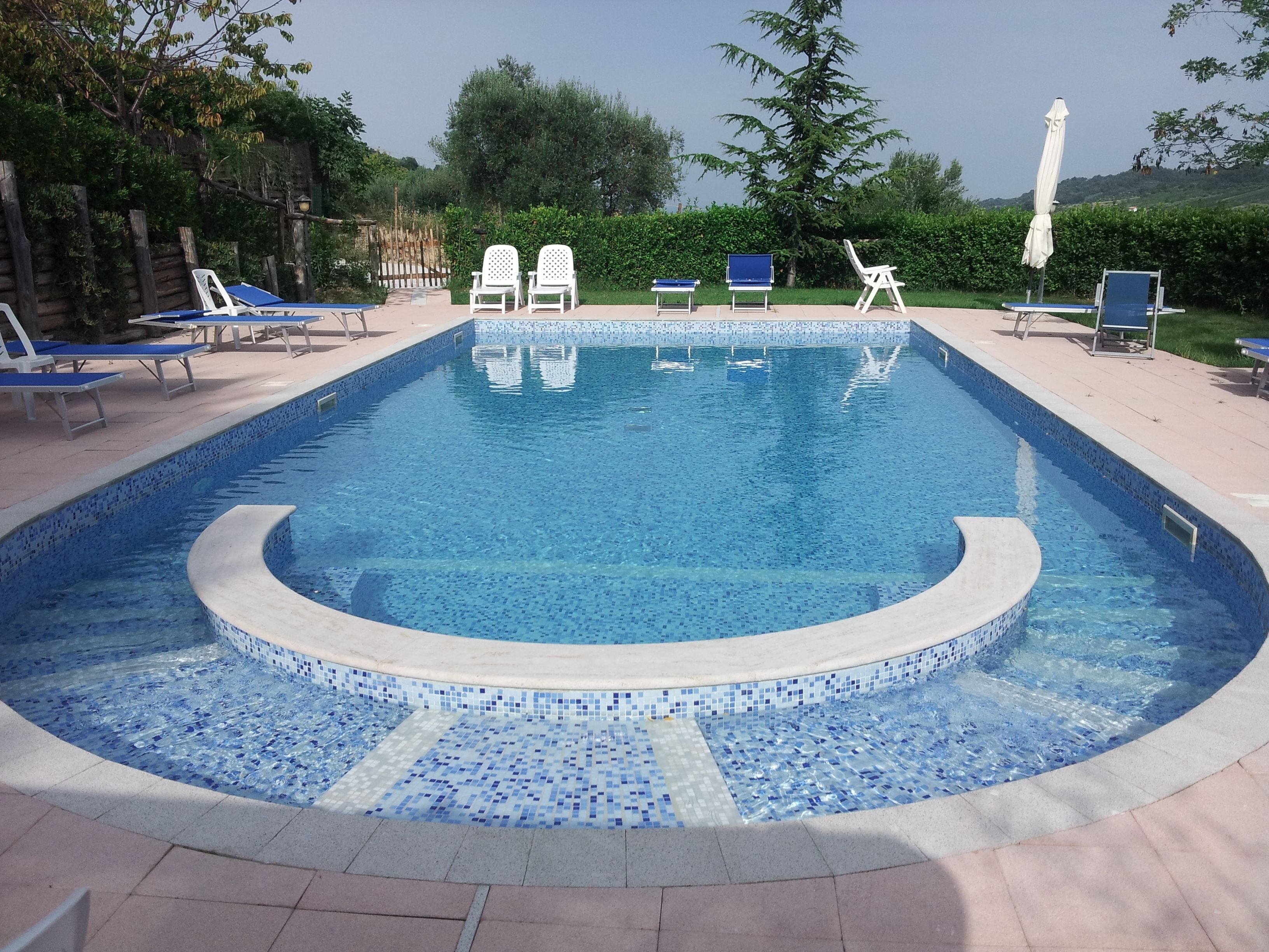 A rectangular swimming pool with a tiled edge, surrounded by lounge chairs and umbrellas.
