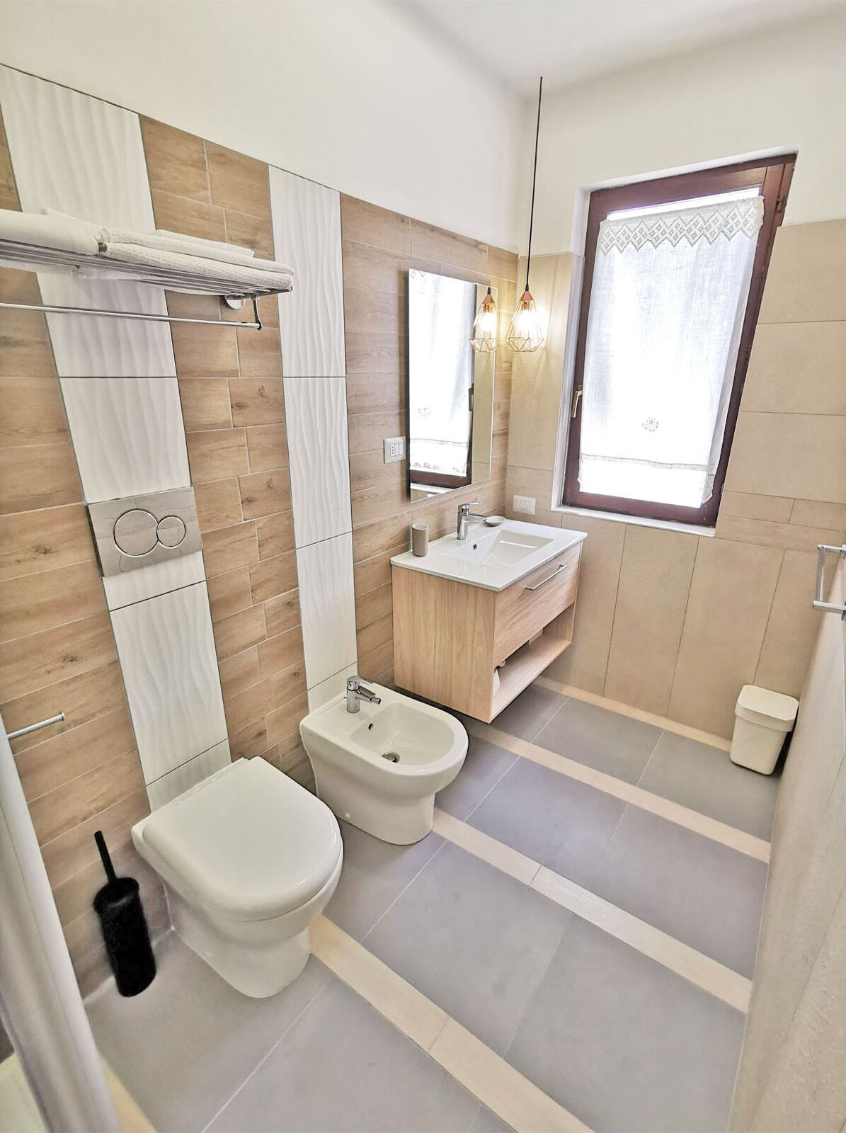 A modern bathroom with a toilet, bidet, vanity, and a large mirror.