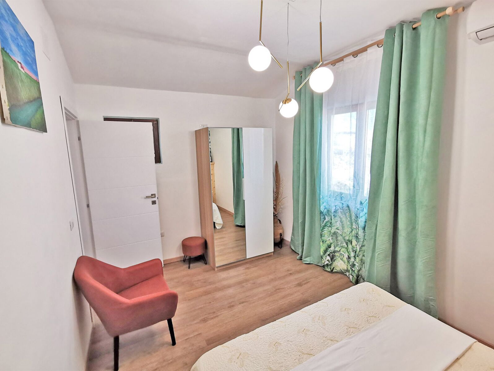 A modern bedroom with a bed, a red chair, a mirror, and green curtains.