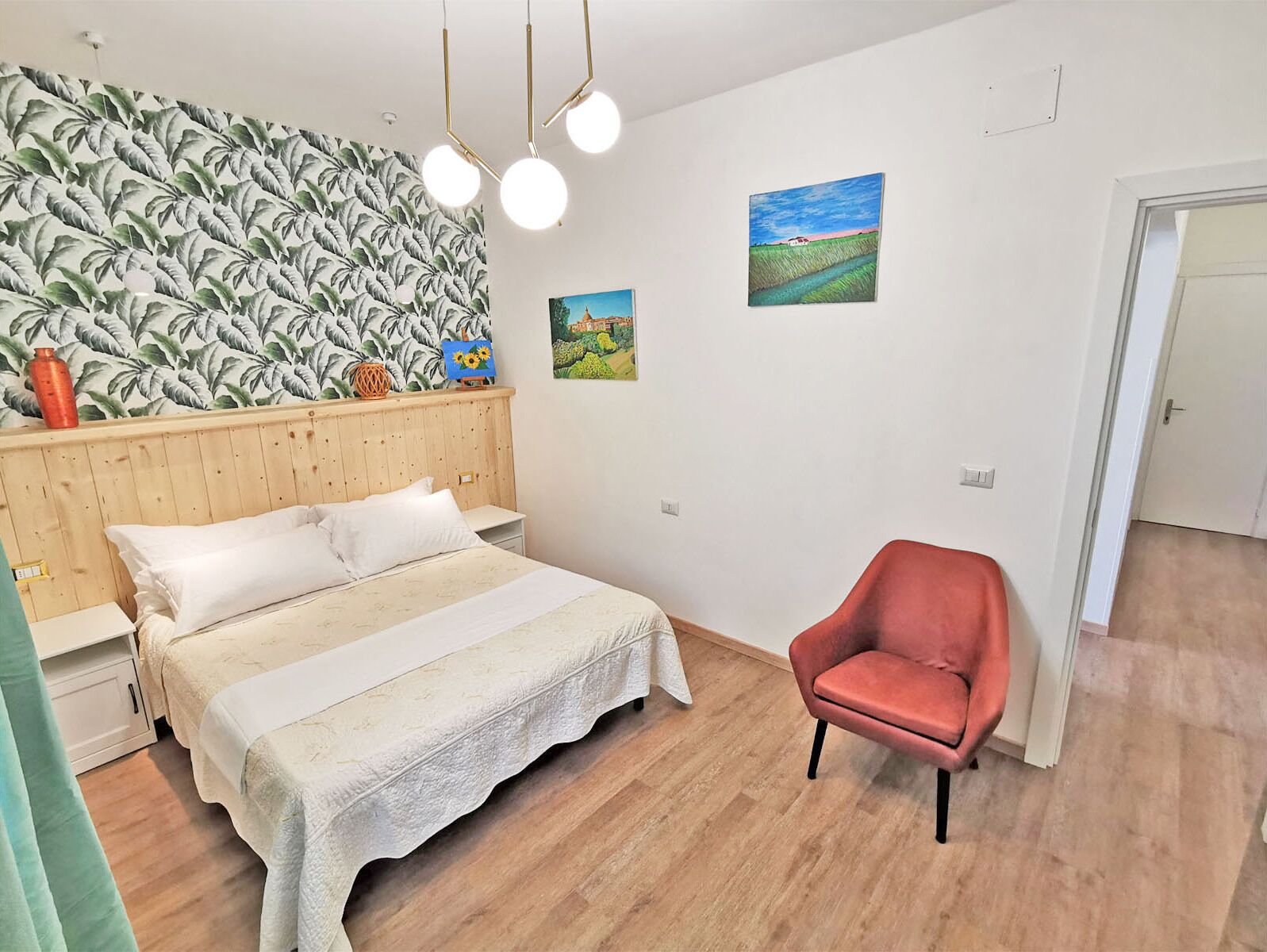 A bedroom with a bed, a red chair, a wooden headboard, and two wall-mounted paintings.