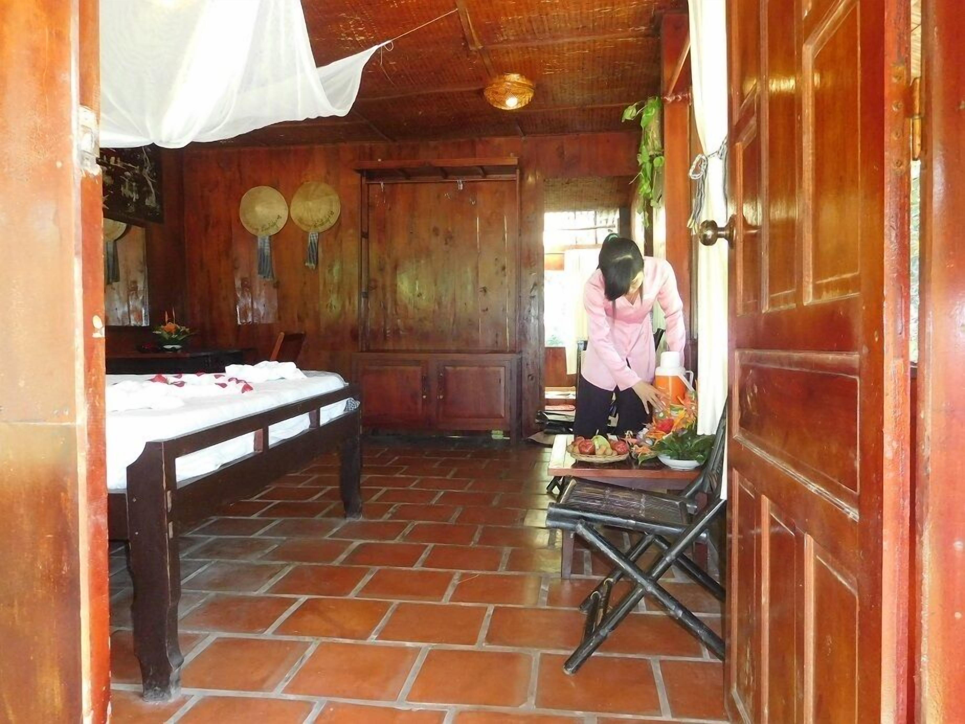 A room with a bed, a table with fruits, and a person preparing food.